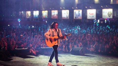 Ken Hensley on stage with an acoustic guitar, before a crowd lit with phone lights.
